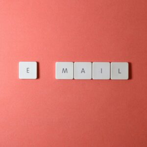 Flat lay of keyboard letter tiles spelling 'email' on coral backdrop.